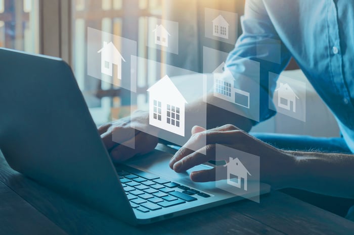 A homebuyer searches properties on a laptop. Gray boxes with white icons represent the properties he is viewing.